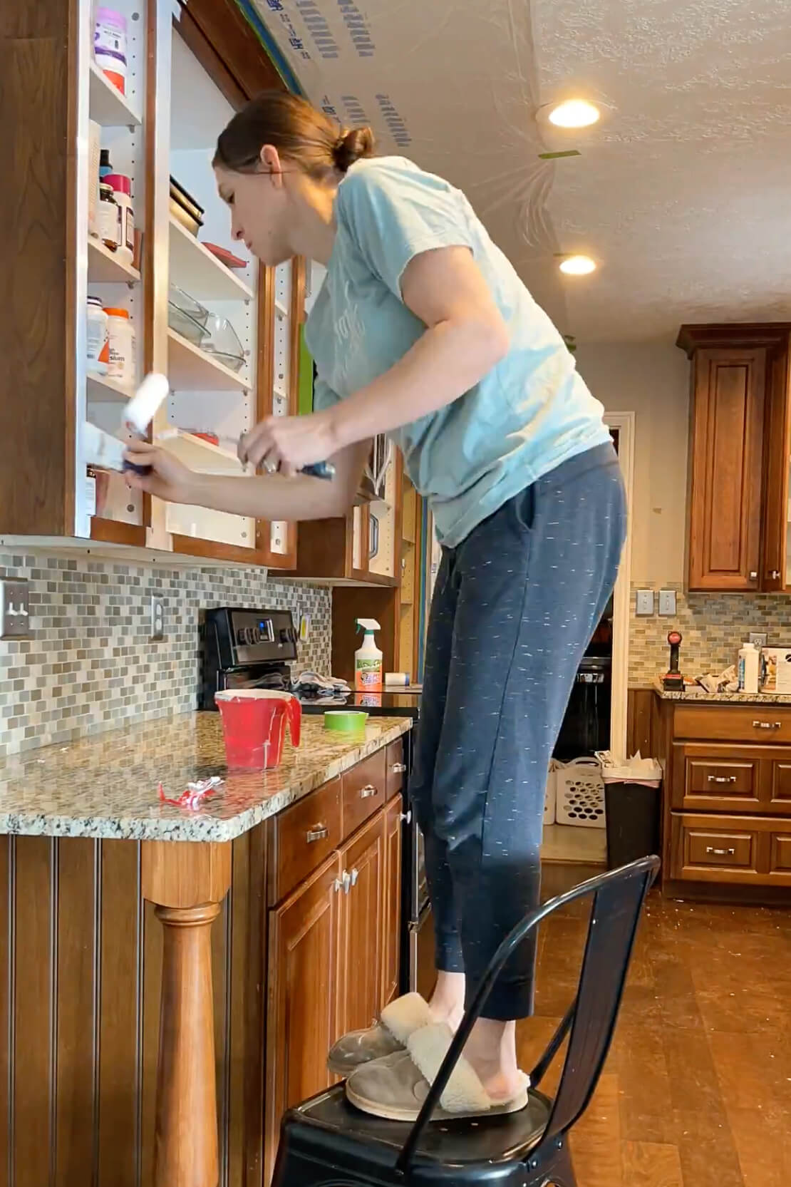 Using a roller and a paintbrush to apply cabinet paint to the face frames of the kitchen cabinets.